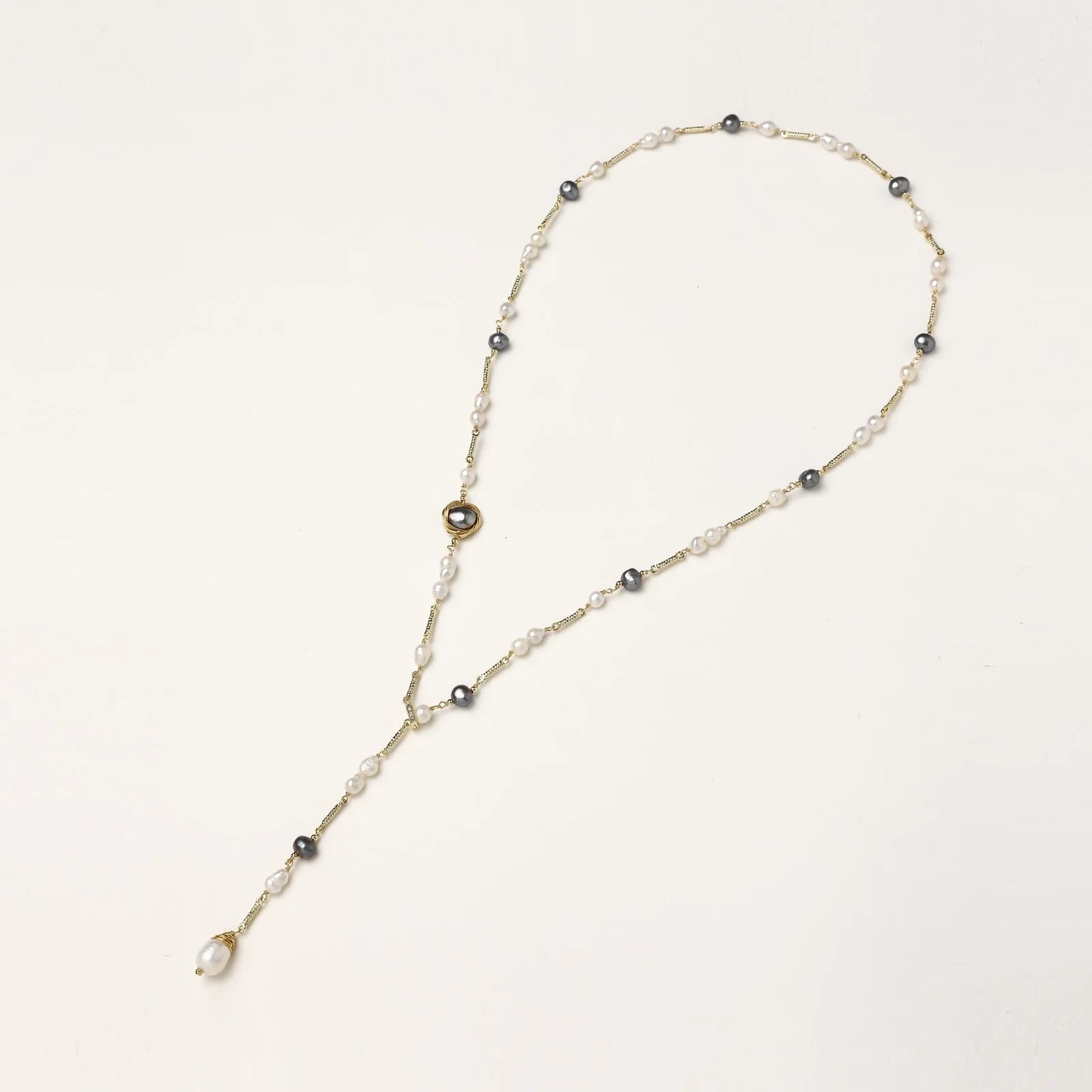 Y-shaped gold-plated necklace with white and gray freshwater pearls on cream background, showing adjustable drop design.