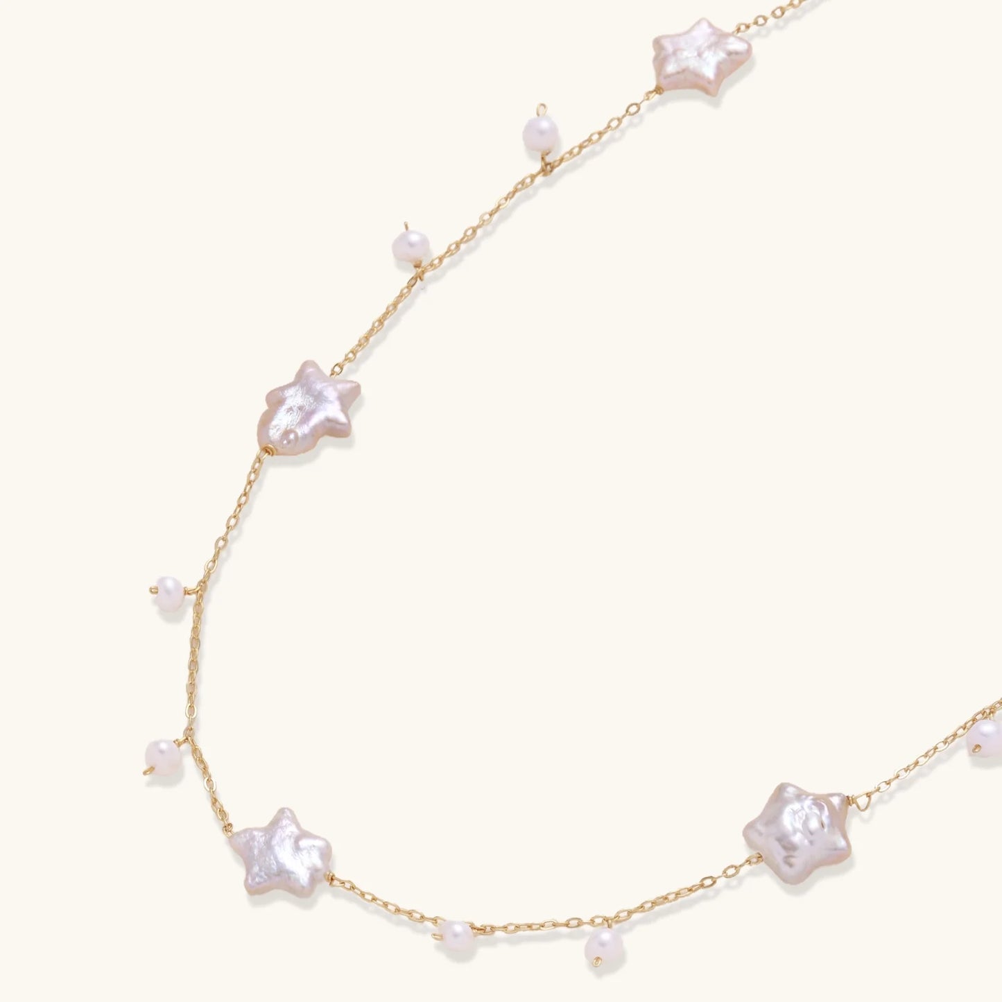 Gold vermeil chain with iridescent star-shaped baroque pearls and small round freshwater pearl drops on cream background.