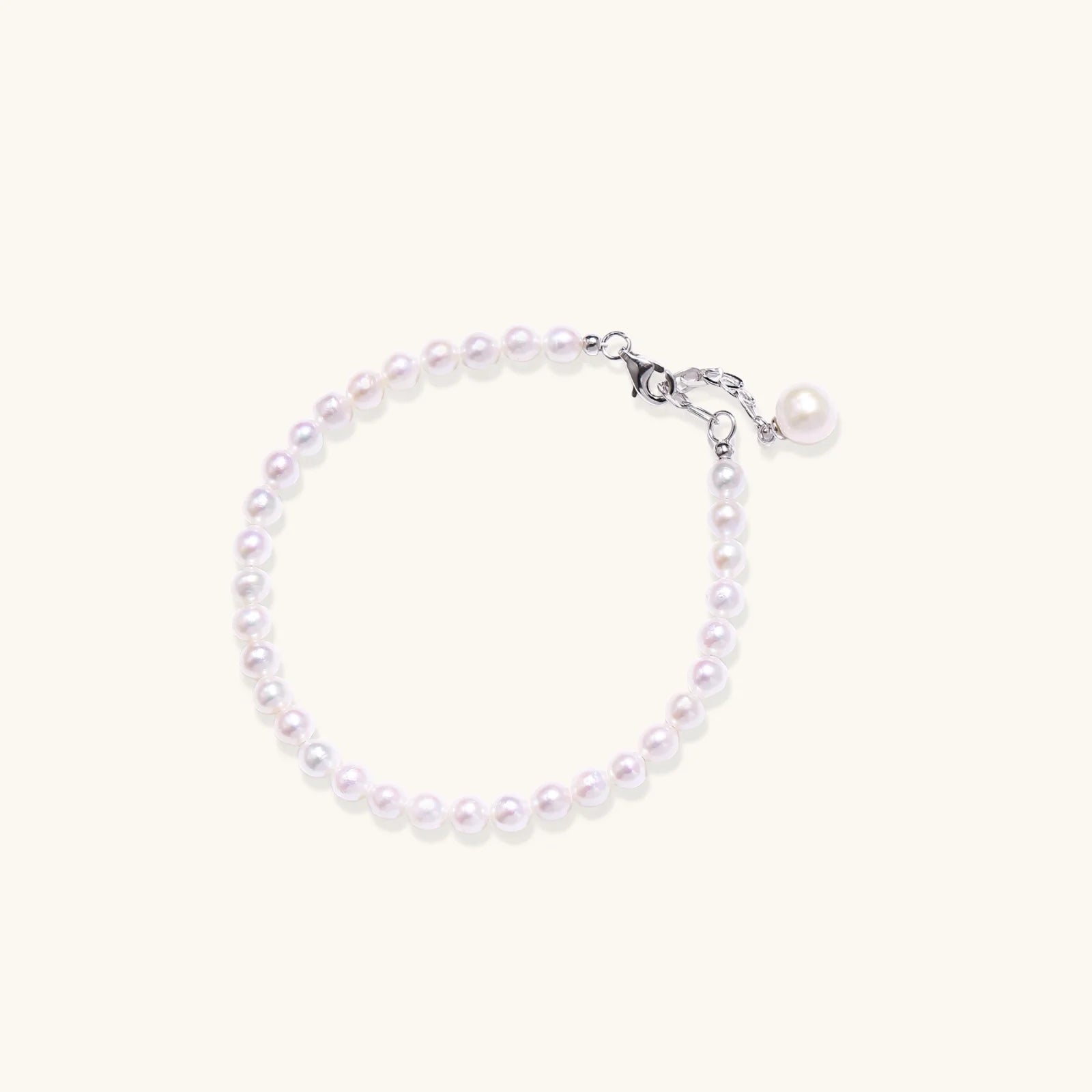 Delicate freshwater pearl bracelet with rhodium-plated silver clasp and single pearl drop charm on cream background