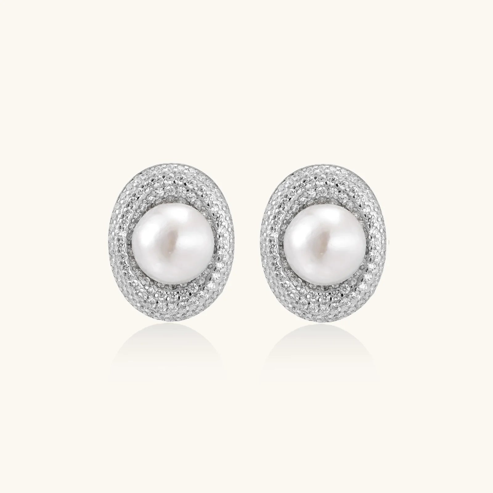 Oval rhodium-plated silver studs featuring freshwater pearls surrounded by pavé crystal halo on white background
