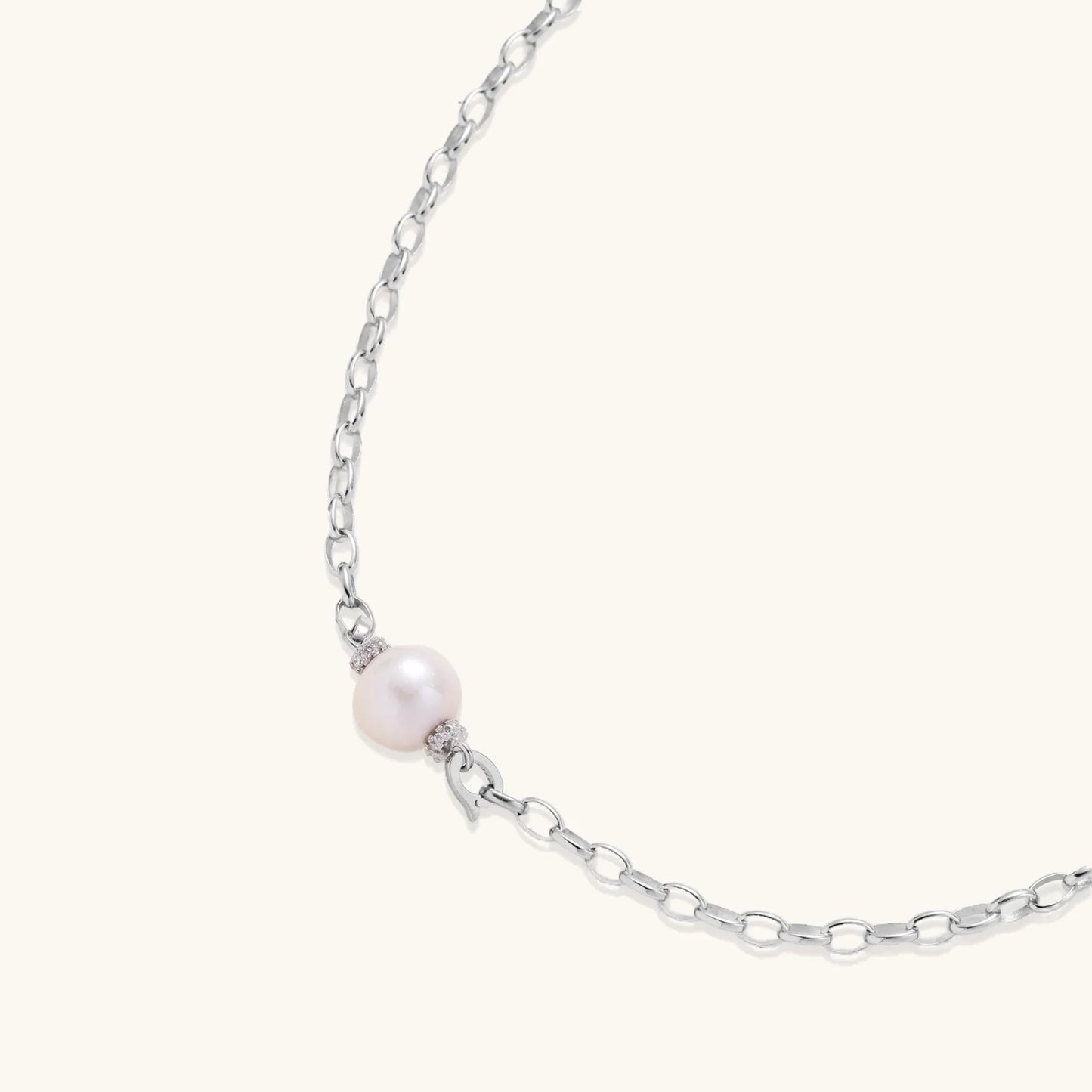 Dainty rhodium-plated silver chain necklace with centered 10mm freshwater pearl and crystal accents on cream background