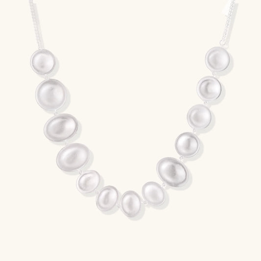 Graduated pearl-finish silver discs forming an organic bubble bib necklace on delicate chain against cream background.