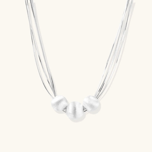 Sterling silver multi-strand necklace with three brushed round beads on cream background