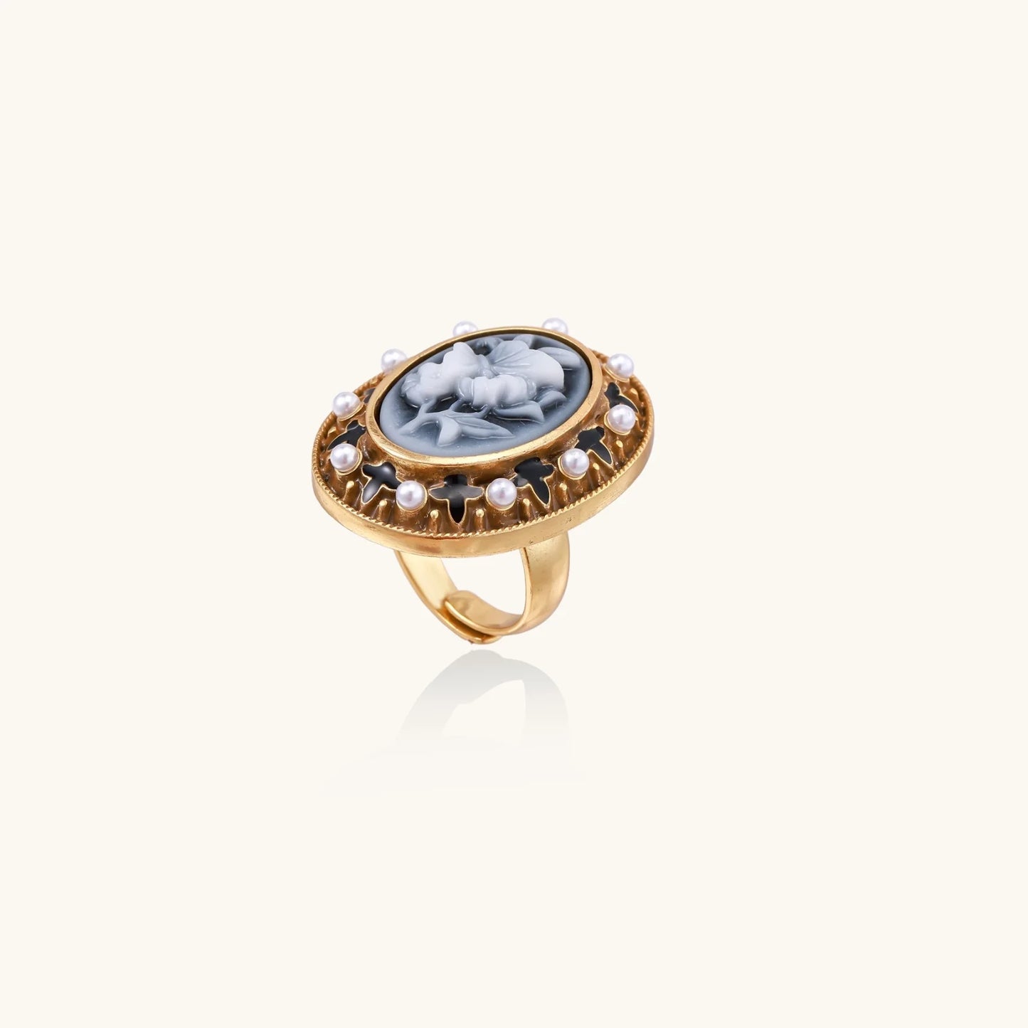 Gold-plated ring with oval blue floral cameo, pearl accents, and black enamel detailing on white background.