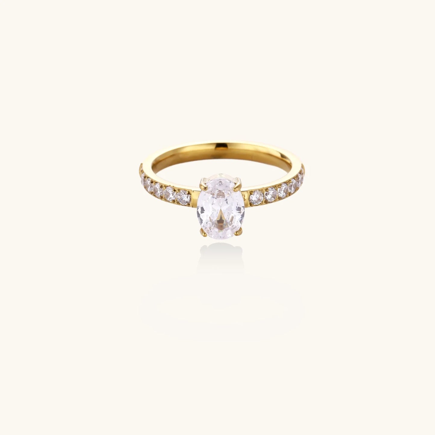 Gold-plated solitaire ring with oval zirconia center stone and pavé band on cream background
