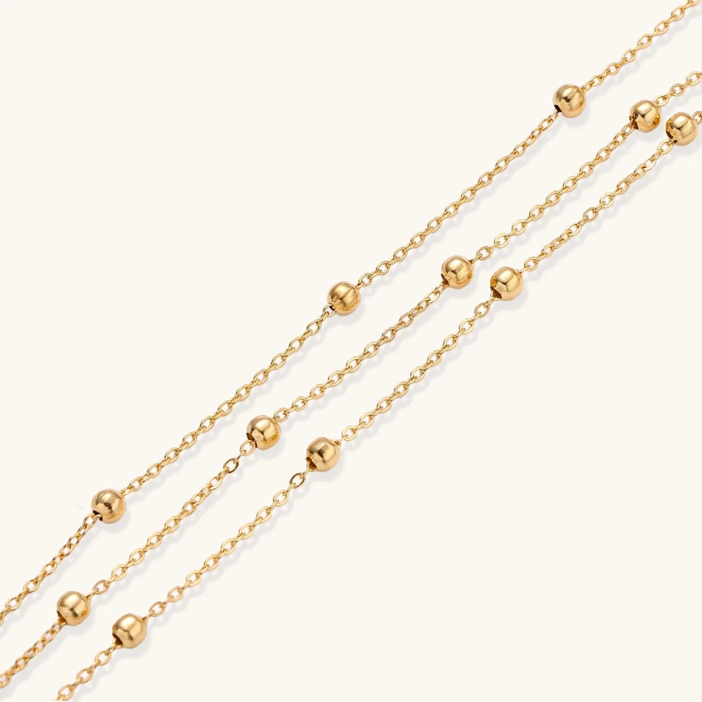 Three-strand gold-plated bracelet with clustered ball beads and adjustable clasp on cream background